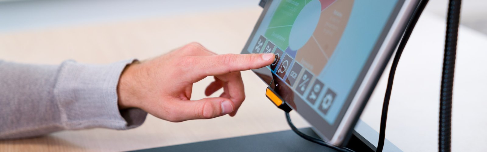 A person's hand touches an on-screen toolbar on a mounted display in an accessible workplace.